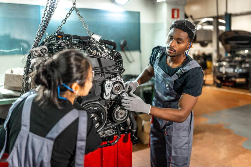Two mechanics work to rebuild an engine in an auto repair shop, carefully inspecting engine components for repair and restoration.