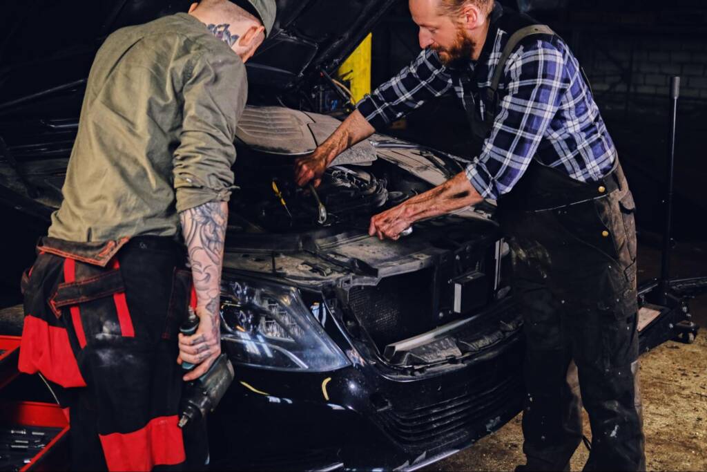 Two bearded mechanics inspect car engine parts during a dyno car tuning session.