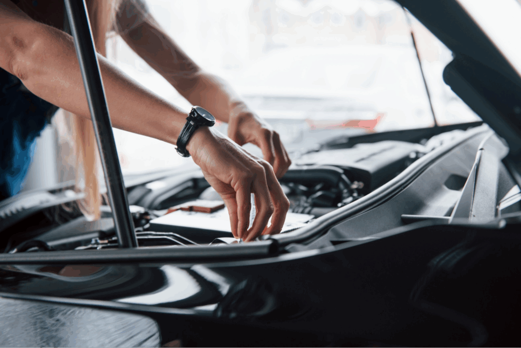 A woman’s hands working under the hood of a car