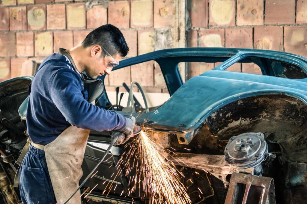 A young male mechanic engaged in car restoration, welding the body of a vintage vehicle in a shop.