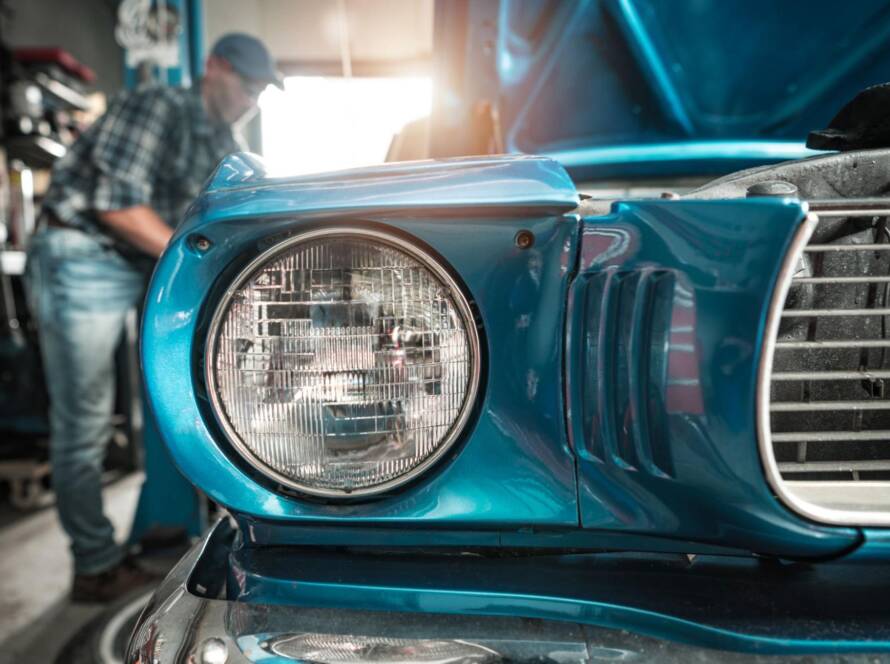 Classic car restorer applies final touches to a freshly restored blue vintage vehicle inside the workshop.