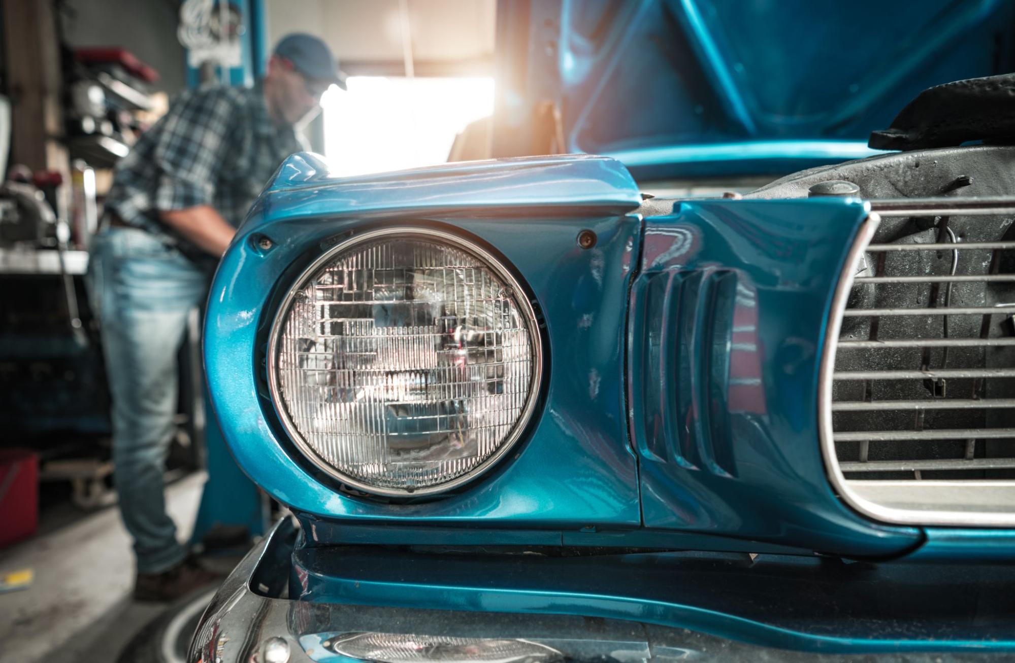 Classic car restorer applies final touches to a freshly restored blue vintage vehicle inside the workshop.