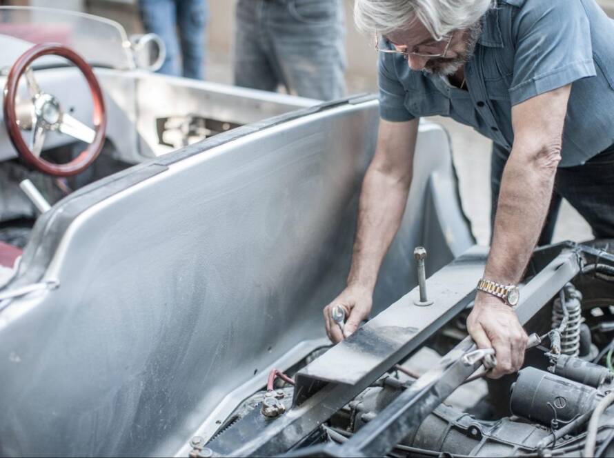 A senior mechanic performs an engine rebuild on an older vehicle.
