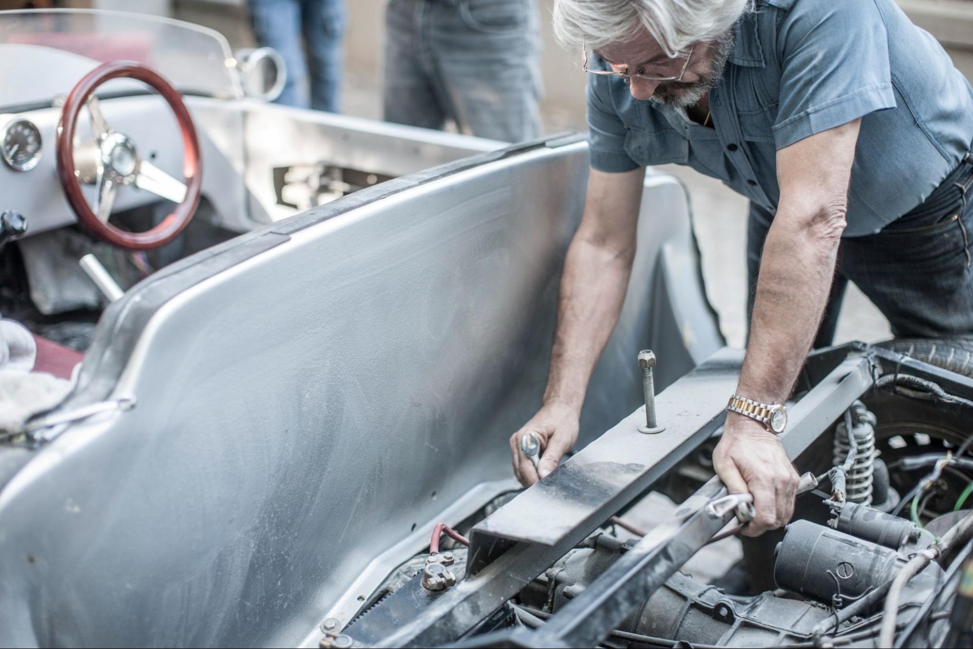 A senior mechanic performs an engine rebuild on an older vehicle.