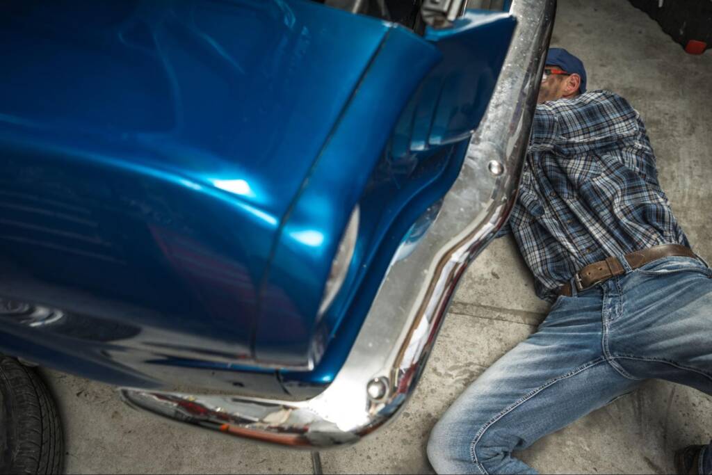A mechanic under the hood fixing the engine of a blue vintage car.