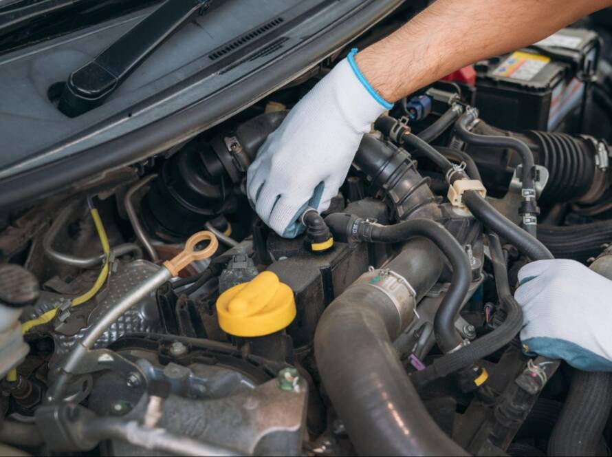 A mechanic inspects a car engine during a transmission service check.