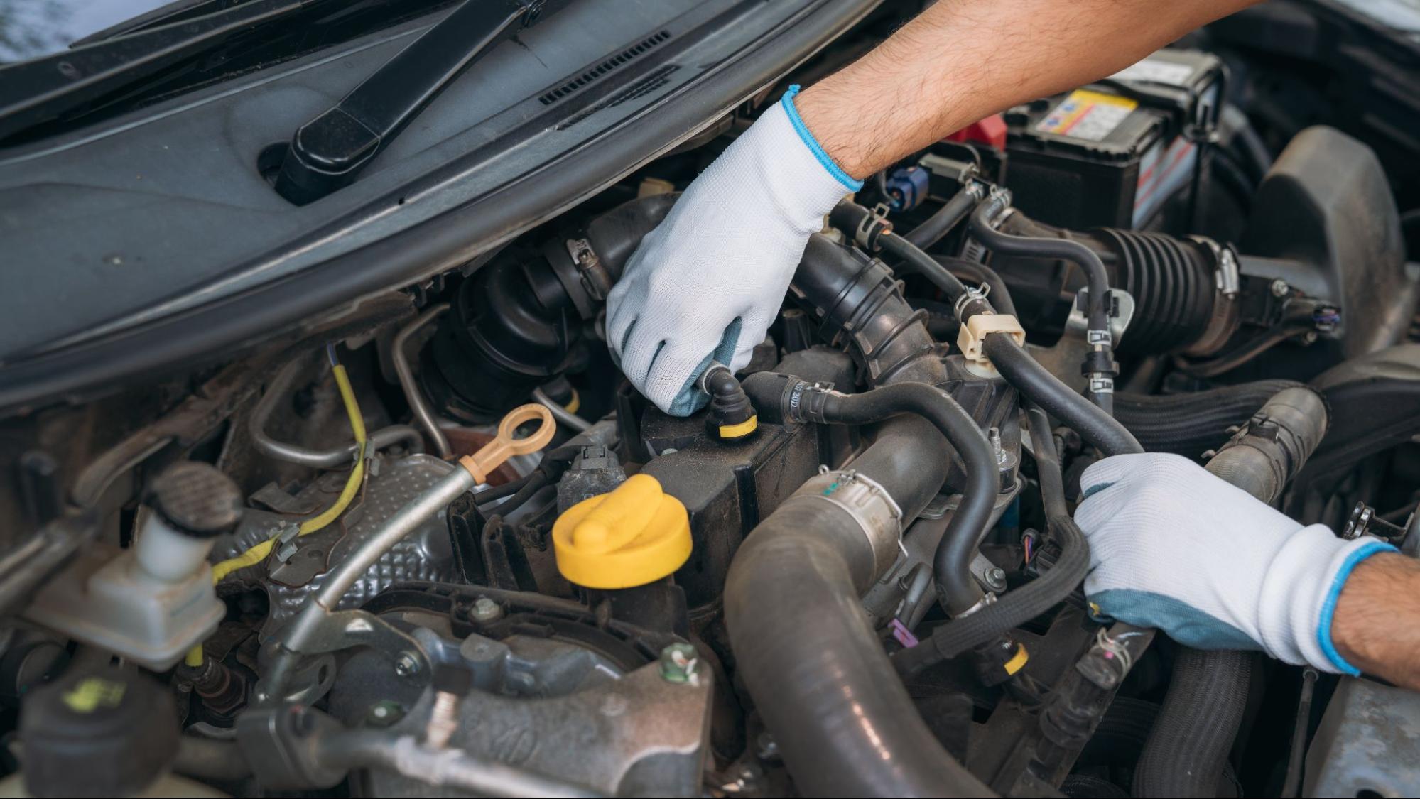 A mechanic inspects a car engine during a transmission service check.