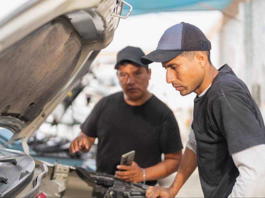 Two automotive technicians inspect a car engine during a diagnostic check in a repair shop.