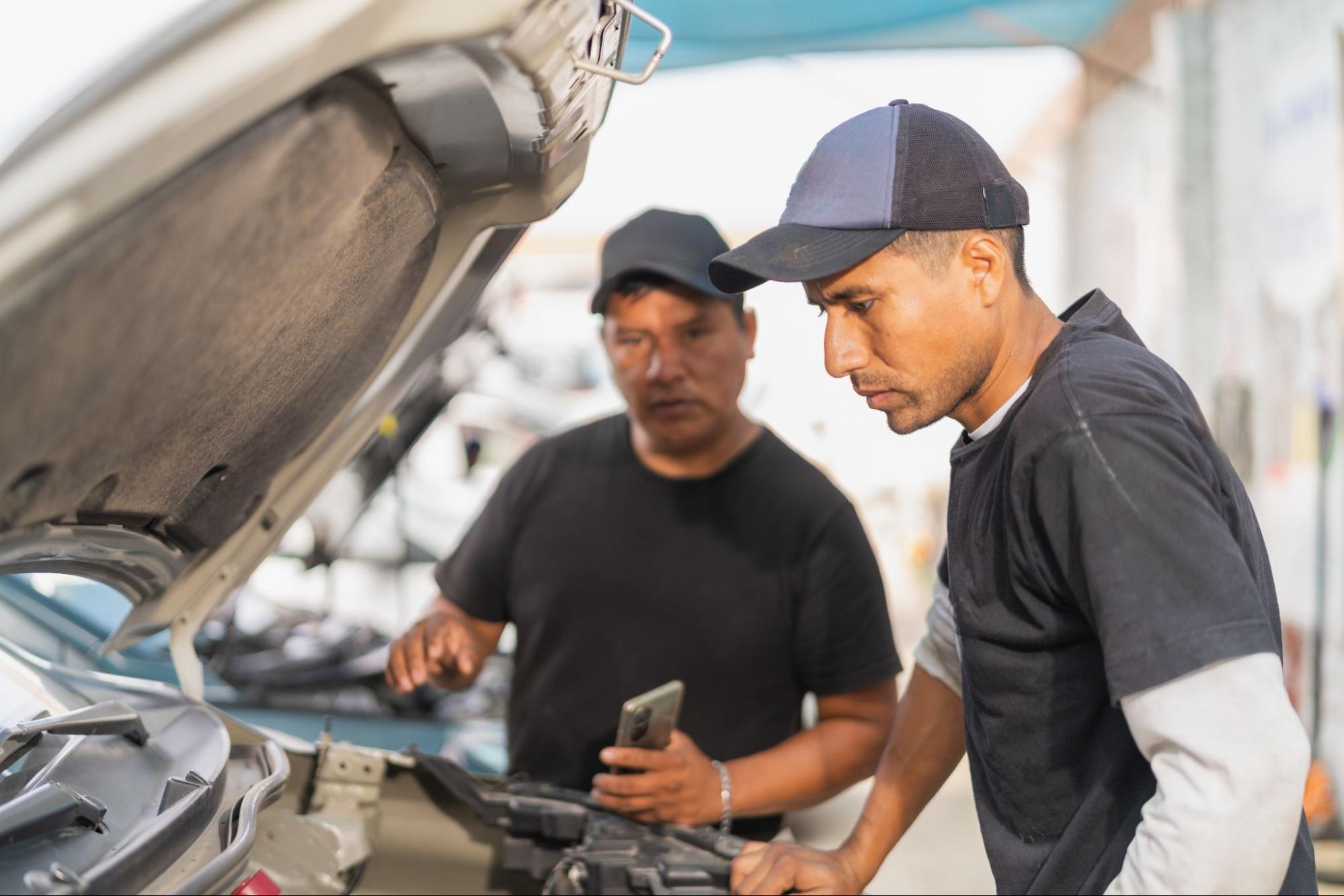 Two automotive technicians inspect a car engine during a diagnostic check in a repair shop.