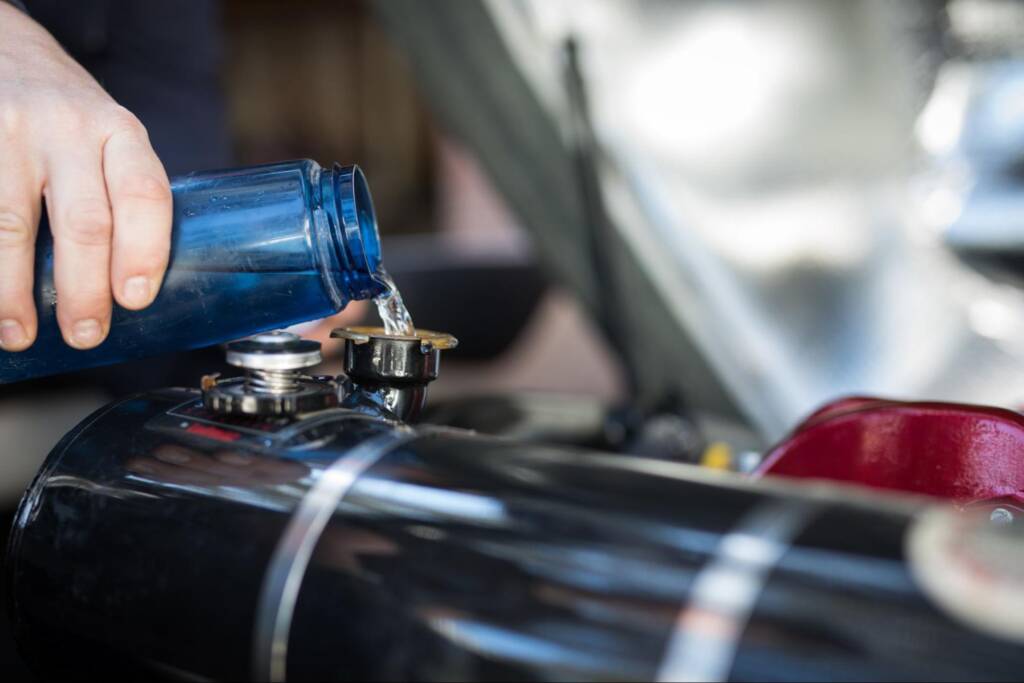 A hand pouring motor oil into a car engine during routine maintenance.